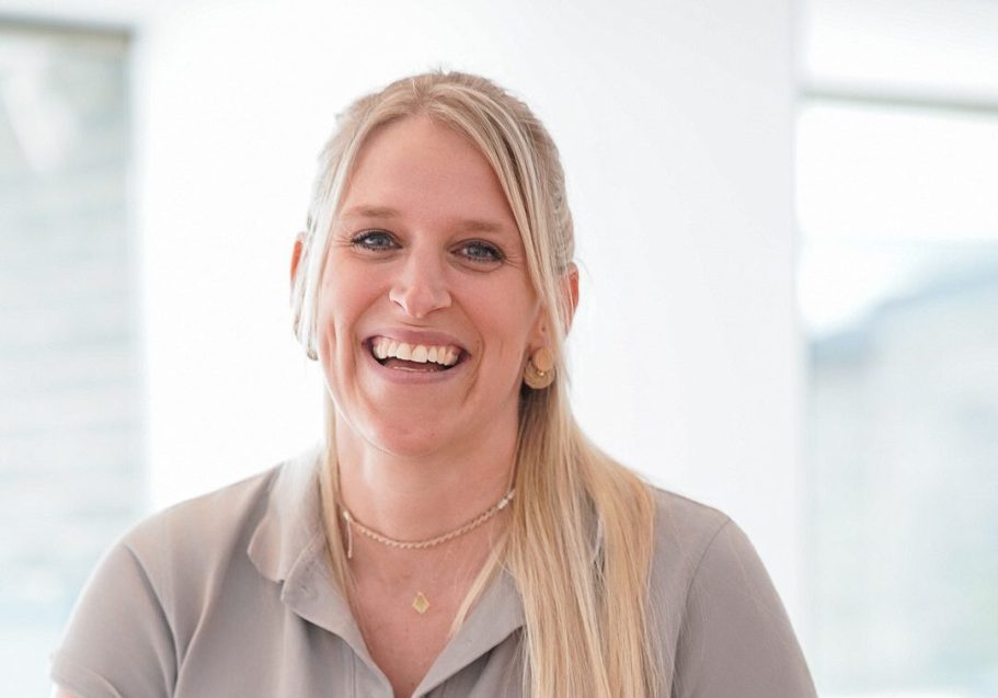 Lächelnde Frau mit langen blonden Haaren, trägt ein graues Shirt.