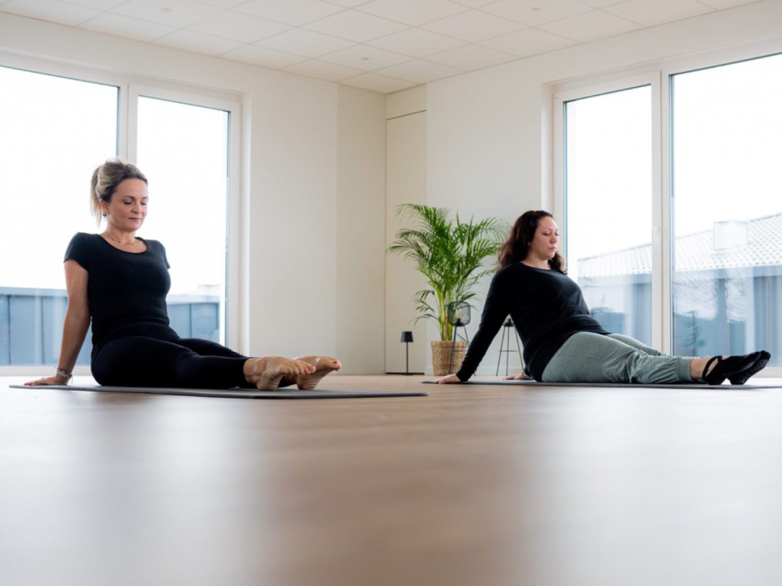 Zwei Frauen in bequemer Kleidung praktizieren Yoga in einem hellen Raum.