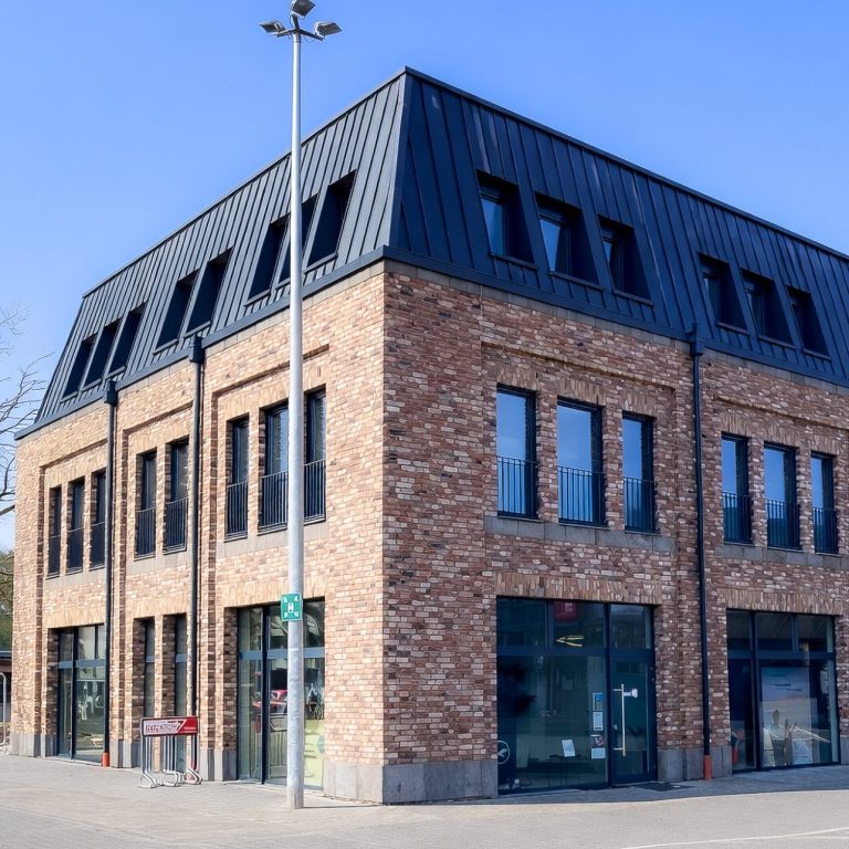 Moderner Backsteinbau mit Dachfenstern und großen Fenstern, klare Linien und blauer Himmel.