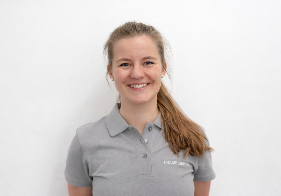 Junge Frau mit langen, blonden Haaren in einem grauen Polohemd, lächelt freundlich.